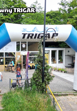 Meta biegu charytatywnego. W tle budynek kawiarni w środku parku. Po prawej duża szachownica i dużymi pionkami.