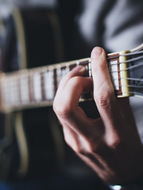 Zdjęcie, zbliżenie gryfu gitary, oraz grających dłoni