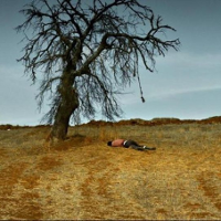 Mężczyzna leżacy pod drzewem na łące. Na gałęzi drzewa wisi sznur.
