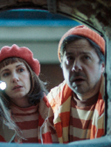 Dziewczynka, kobieta i mężczyzna ubrani w podobne stroje i czerwone nakrycia na głowie zaglądają do wąskiego pomieszczenia.