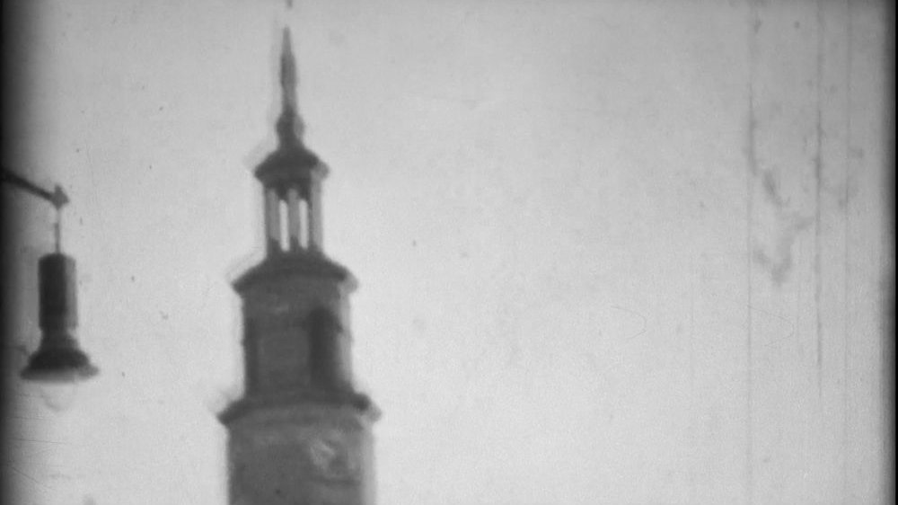 Biało-czarny i poruszony kadr z filmu przedstawiający wieżę Ratusza Poznańskiego.
