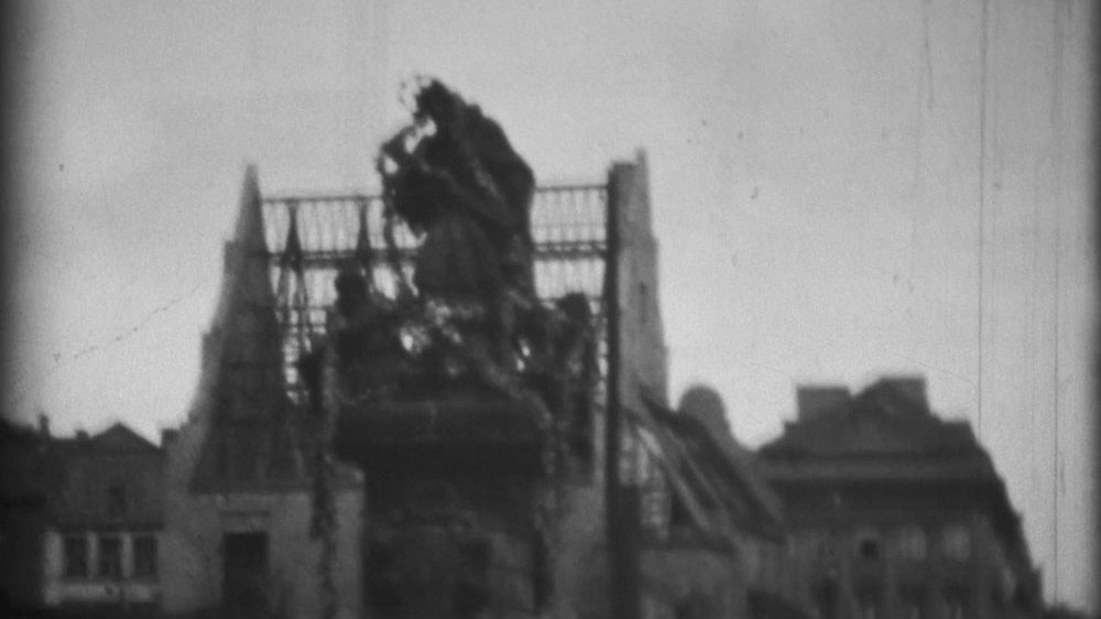 Kadr ze starego filmu. Z przodu figura św. Jana Nepomucena na Starym Rynku. Z tyłu zrujnowane w czasie wojny dachy kamienic.