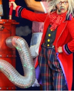 zdjęcie przedstawia postać w kolorowym stroju stojącą przy machinie przypominjącej rakietę