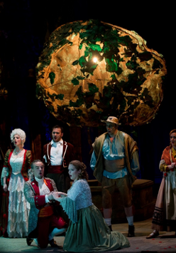 Na scenie aktorzy w kostiumach z epoki, na pierwszym planie klęczą mężczyzna i kobieta, za nimi rząd innych postaci. Wszyscy śpiewają.