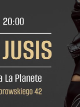 Zdjęcie przedstawia kobietę w kreatywnej, nietypowej pozie. Jej twarz jest ukryta za białymi krótkimi włosami. Ma na sobie skórzaną kurtkę i obcisły kombinezon.