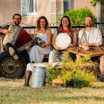 Cztery osoby z ludowymi instrumentami siedzą na drewnianej przyczepie.