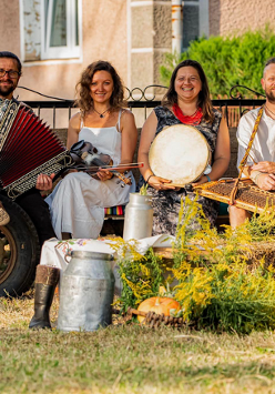Cztery osoby z ludowymi instrumentami siedzą na drewnianej przyczepie.