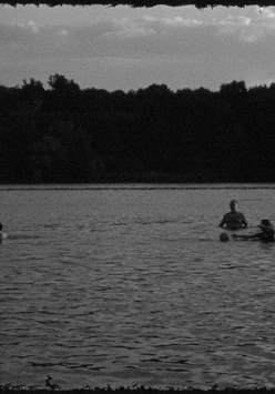 Czarno-biała fotografia kąpiących sie ludzi w jeziorze.