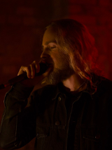 Na ciemnym tle osoba, która śpiewa do mikrofonu