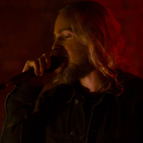 Na ciemnym tle osoba, która śpiewa do mikrofonu