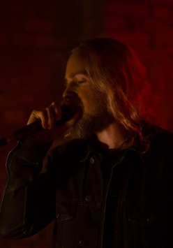 Na ciemnym tle osoba, która śpiewa do mikrofonu