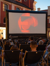 Zdjęcie, Wolny Dziedziniec Urzędu Miasta Poznania, na dziedzińcu wyświetlany jest film, przed ekranem rozłożono leżaki, na których siedzą ludzie.