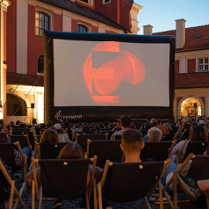 Zdjęcie, Wolny Dziedziniec Urzędu Miasta Poznania, na dziedzińcu wyświetlany jest film, przed ekranem rozłożono leżaki, na których siedzą ludzie.