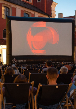 Zdjęcie, Wolny Dziedziniec Urzędu Miasta Poznania, na dziedzińcu wyświetlany jest film, przed ekranem rozłożono leżaki, na których siedzą ludzie.