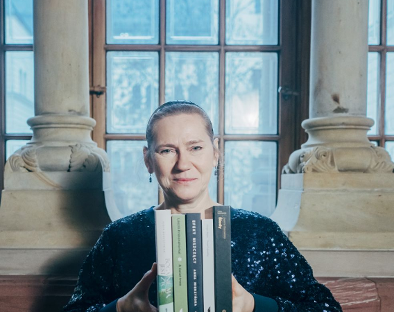 Kobieta prezentuje zestaw książek siedząc na tle okna.