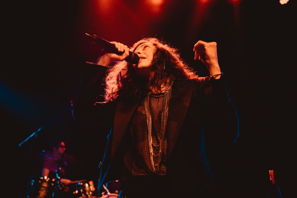 Kobieta śpiewa do mikrofonu z rękoma uniesionymi w górze.