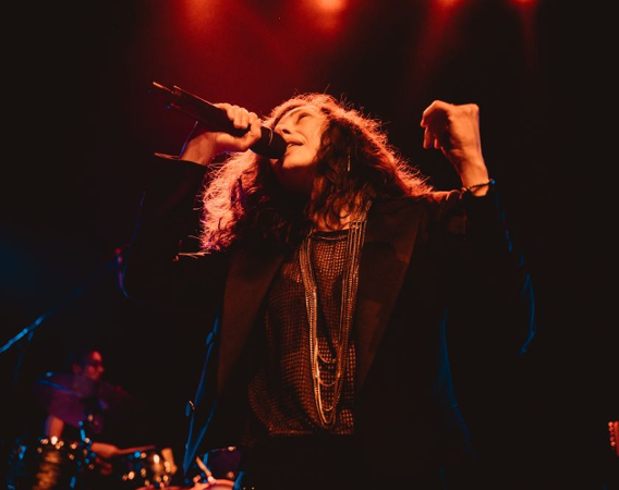 Kobieta śpiewa do mikrofonu z rękoma uniesionymi w górze.