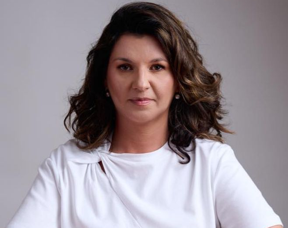 Kobieta w białej bluzce siedzi przy stole, na którym leży książka.