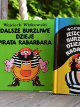 Trzy ksiązki stojące obok siebie z kolorowymi okładkami z piratem. W tle zielone drzewa.