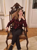 Zdjęcie artystki, która siedzi na drewnianym, tapicerowanym krześle.