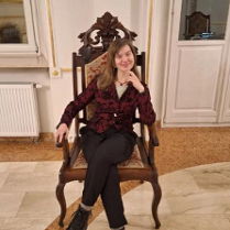 Zdjęcie artystki, która siedzi na drewnianym, tapicerowanym krześle.