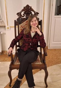 Zdjęcie artystki, która siedzi na drewnianym, tapicerowanym krześle.