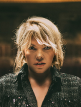 Zdjęcie Anny Dąbrowskiej od frontu. W tle rozmyte zaciemnione pomieszczenie.