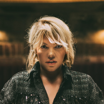 Zdjęcie Anny Dąbrowskiej od frontu. W tle rozmyte zaciemnione pomieszczenie.