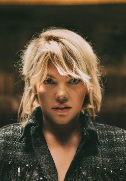 Zdjęcie Anny Dąbrowskiej od frontu. W tle rozmyte zaciemnione pomieszczenie.