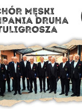 Grupa chórzystów pozuje do zdjęcia w czarnych garniturach, nad nimi informacje o koncercie.