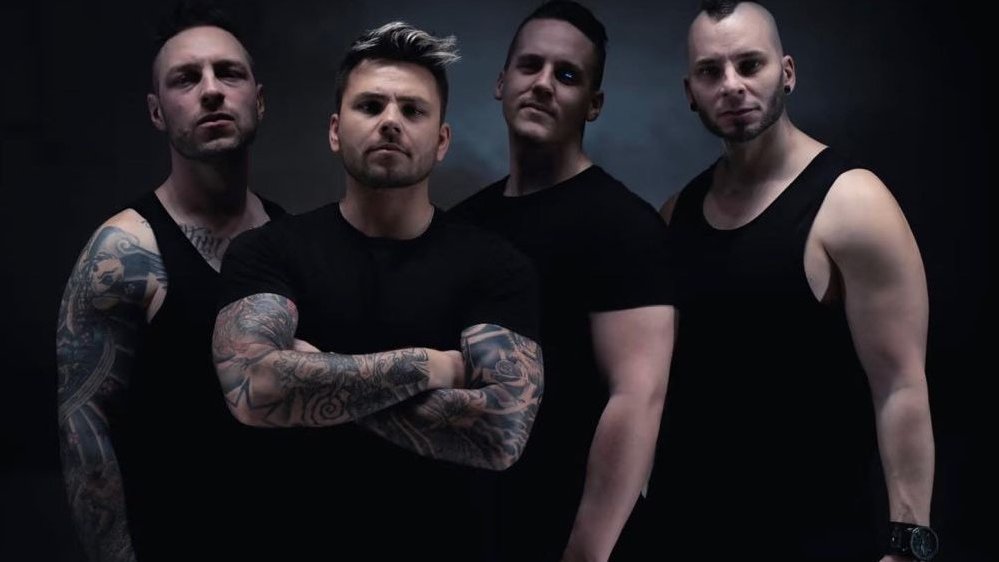 Czworo mężczyzn pozuje do zdjęcia na ciemnym tle. Wszyscy mają na sobie czarne koszulki, dwóch z nich nosi widoczne tatuaże.