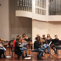 Na obrazku widać grupę muzyków. Wszyscy grają na skrzypcach.