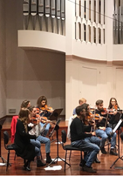 Na obrazku widać grupę muzyków. Wszyscy grają na skrzypcach.