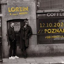 Obraz przedstawia dwóch mężczyzn stojących na chodniku przed ceglanym murem. Na ścianie znajduje się napis "LOREIN" z żółtymi literami. Jest też napis "COFFEE" i kolejny napis "12.10.2024 // POZNAN // POD MINOGĄ // UGP". Mężczyźni mają na sobie zwykłe ubrania i wydają się patrzeć na coś poza kamerą. Obraz jest czarno-biały, a oświetlenie jest stosunkowo słabe.