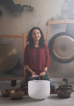Kobieta nachyla się nad misą do grania, za nią stoją dwa gongi.
