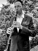 Czarno-białe zdjęcie, muzyk gra na flecie w plenerze.