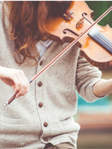 Młoda kobieta gra na skrzypcach wśród przyrody.