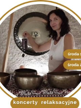 Kobieta w średnim wieku, w białej koszule, z czarnymi kręconymi włosami. Stoi przy rozłozonych złotych misach.