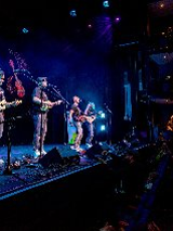 Zdjęcie przedstawia czterech muzyków występujących na scenie, grających na ukulele.