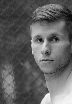 Czarno-białe zdjęcie przedstawia twarz tancerza Daniela Michny, patrzącego wprost w kierunku, z którego wykonano zdjęcie.