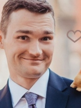 Zdjęcie przedstawia uśmiechniętego mężczyznę w marynarce i koszuli z krawatem, mającego na lewym ramieniu maskotkę wiewiórki.