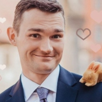 Zdjęcie przedstawia uśmiechniętego mężczyznę w marynarce i koszuli z krawatem, mającego na lewym ramieniu maskotkę wiewiórki.