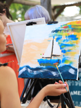 Osoba maluje obraz na sztaludze farbami akrylowymi.