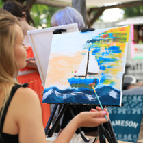 Osoba maluje obraz na sztaludze farbami akrylowymi.