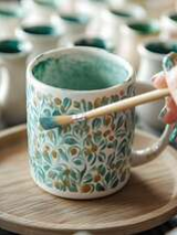 Ceramiczny kubek i malujący go pędzel.