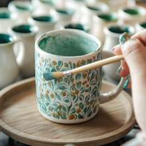 Ceramiczny kubek i malujący go pędzel.