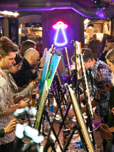 Grupa osób maluje obrazy, siedząc w pomieszczeniu o ceglanych ścianach.