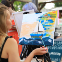 Osoba maluje obraz na sztaludze farbami akrylowymi.