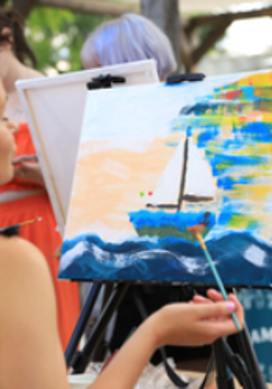 Osoba maluje obraz na sztaludze farbami akrylowymi.