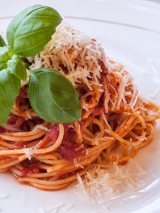 Makaron z sosem pomidorowym, posypany tartym serem, udekorowany liśćmi bazylii.